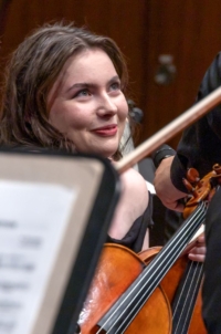 eine junge Frau mit Geige in der Hand und blickt fröhlich