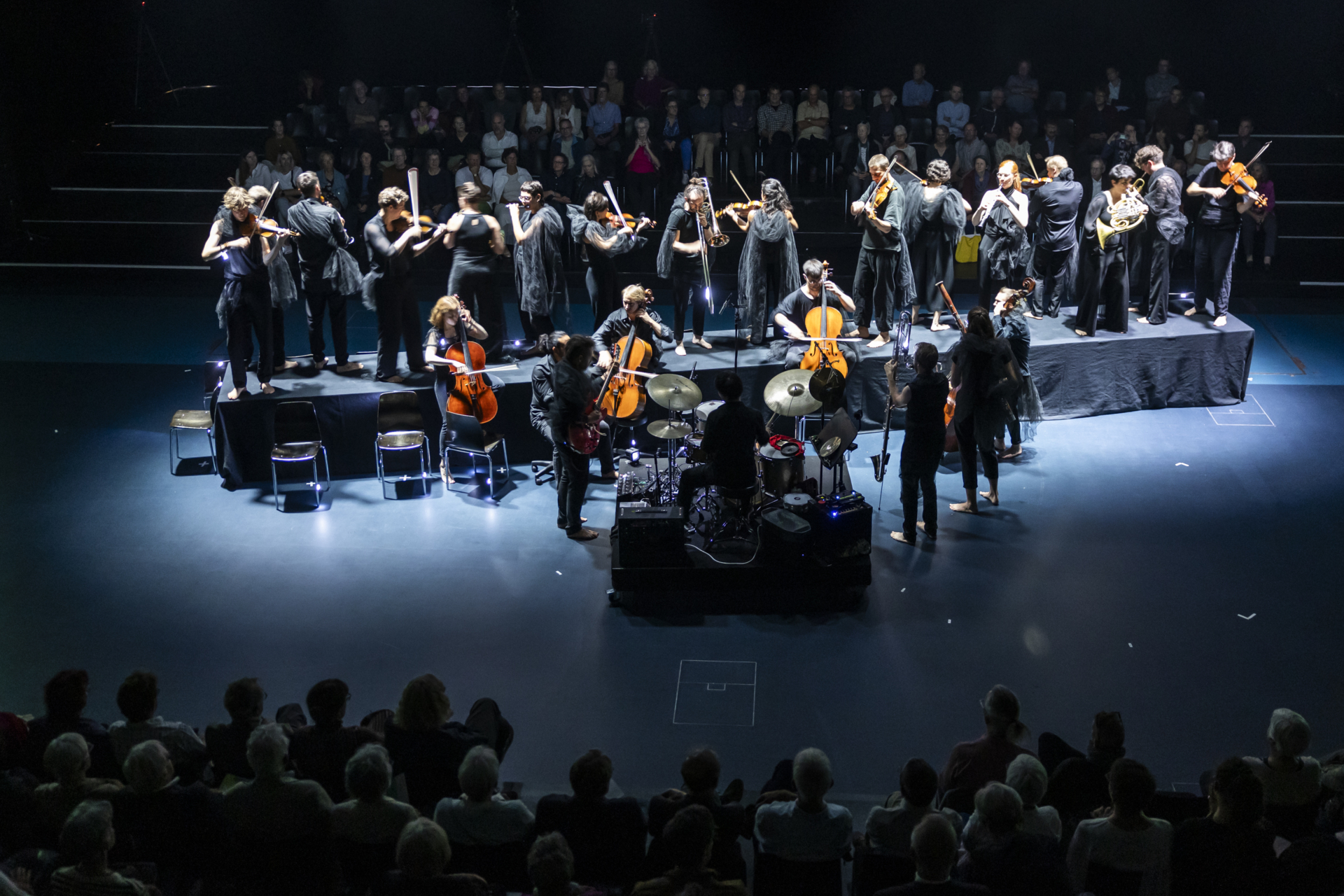 Orchestermusiker mit ihren Instrumenten auf einem diagonal im Raum liegenden "Laufsteg", davor ein Schlagzeug... #freebruckner, Luzern Festival 2024, Foto: Patrick Hürlimann